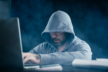 A computer hacker is typing on a laptop in a smoky room. Dark background