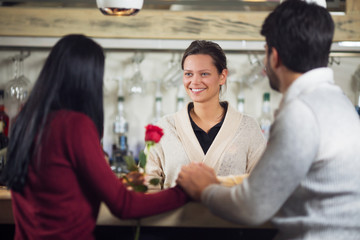 Young beautiful woman serving coffee to  couple in cafe
