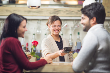 Young and beautiful barista serving coffee to couple