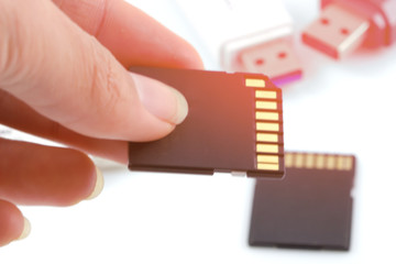 Hand holds SD card, memory card, (camera card) against usb, flash drive with sunrise background.