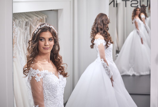 one young bride, looking at self, wearing gown, in mirror image back, front view, bridal salon.