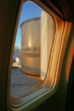 Blick aus einem Flugzeugfenster mit Regentropfen auf eine Passagierbrücke im Morgenlicht