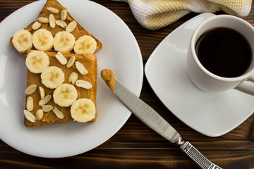 Breakfast: toasts  with peanut paste,banana and coffee on  the brown  wooden background.View from above.