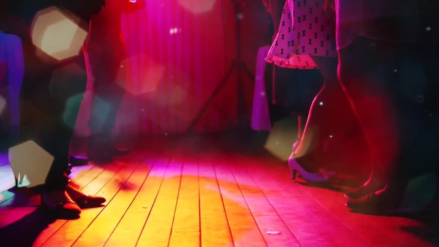 Detail legs and feet of women dancing in a club, Colorful lights illuminate the dance floor.