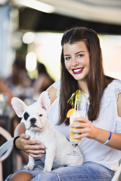 Beautiful young woman with sunglasses sitting in cafe with her adorable French bulldog puppy. People with dogs theme.