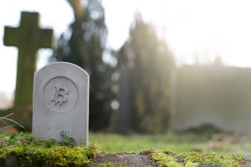 stone monument/tombstone with bitcoin symbol on cementery - sunny blurred background with space for text - economic/financial concept