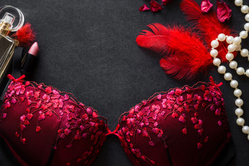 Beautiful lace bra with red feathers, white beads, perfume and lip stick on black background....