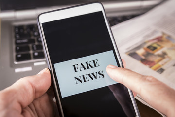 Man's hand holding a smartphone with Fake News words on screen. Fake news, HOAX concept