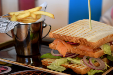 Sandwich with salmon, vegetables and bucket with french fries on a plate