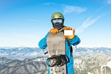 Young snowboarder holding blank ski-pass with beautiful mountains on background