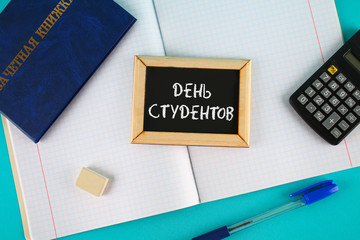 A blue book with an inscription in Russian - a student's record book. Pen, calculator and blank notebooks on a blue background. Inscription in Russian - Students Day.