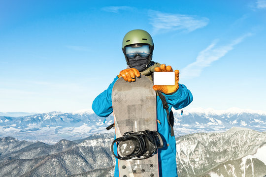 Young snowboarder holding blank ski-pass with beautiful mountains on background