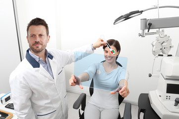 optometrist examining eyesight, woman patient pointing at the hole on plexiglass, ocular dominance test - obrazy, fototapety, plakaty
