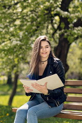 Beautiful caucasian girl student sitting on bench in park reading book