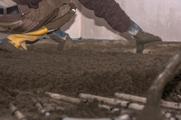 Screed flooring is processed in a residential building. A worker performs sand and cement screed floor over floor heating. Sand and cement floor screed. Concept: construction site and craft