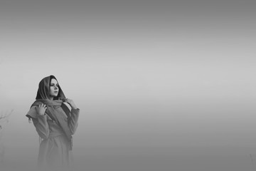 Black and white photo of the girl in a red scarf looking into the distance while standing on a cliff in the fog