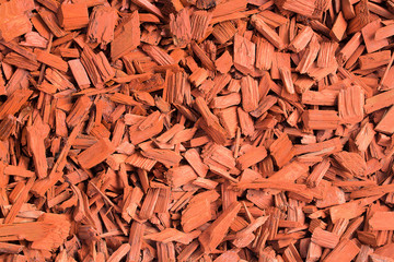 Red wood chips. Natural texture background of red wooden pieces of tree bark. Wood chips, mulch for gardening or natural themes. Full filled frame picture. Landscaping red colored materials.Above view