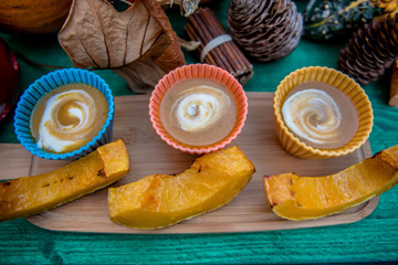 Pumpkin cream soup in three colorful bowls with slices of roasted pumpkin on wooden  green table, autumn and winter favorite food