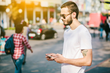 Half length portrait of bearded hipster man dressed in stylish clothes chatting on cell telephone while standing in the street use smart phone during strolling outdoors