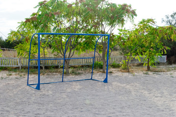 Fototapeta premium Blue football gate without mesh, stand on the sand, against the background of bushes trees, blue sky sun sports rest, playground, children's games