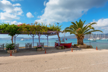 Restaurant tables in Adamas port and palm tree with beautiful view of the Adamas sea port. Milos, Greece.