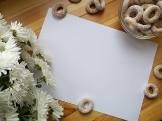 White blank sheet of paper for writing with hands, white flowers and barel lying on wooden table top view
