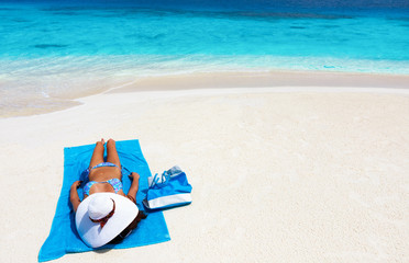 Fototapeta na wymiar Frau im Bikini auf blauem Badetuch liegt am tropischen Strand und genießt ihren Urlaub