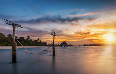 Sonnenuntergang hinter einer tropischen Insel mit Hängematte die im Wind schwingt