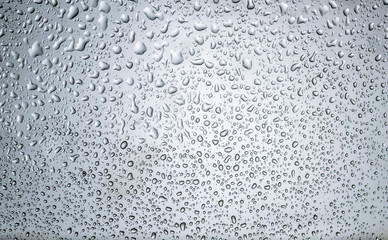 Many small rain water droplets on a clear window glass, macro closeup, blue color