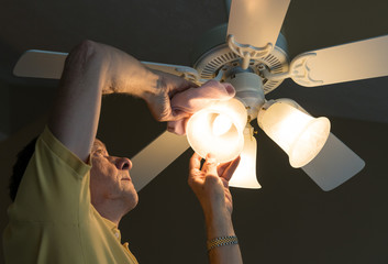 Senior caucasian man dusting lamp shade in ceiling fan and light