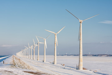 Dutch winter landscape with snowy fields and wind turbines aolong a dike