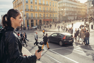 Female professional videographer travel photographer making video in 4K resolution trough of the streets holding 3 axis gimbal stabilizer.Filming with stabilized camera.Travel light equipment