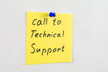 call to technical support note reminder yellow sticker on a white wall pinned with blue pushpin, close up, selective focus