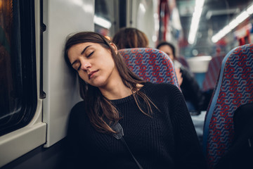 Passenger woman sitting in her seat and sleeping inside a train/bus while traveling.Tired exhausted woman taking a nap in public transportation.Falling asleep during a long ride. - obrazy, fototapety, plakaty