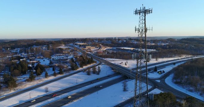 A slow push in aerial establishing shot of a tall cellular tower near a major American interstate in the Winter season.	 	