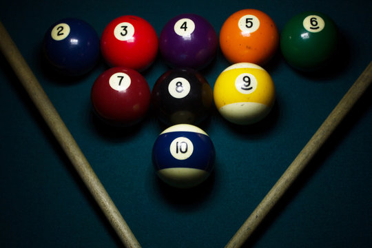 group of billiard balls arranged in triangle with cue sticks on a green billiard table