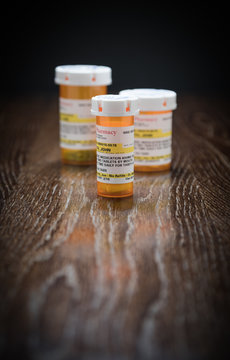 Variety of Non-Proprietary Prescription Medicine Bottles on Reflective Wooden Surface.