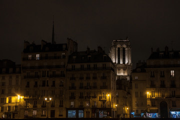 Fototapeta na wymiar Notre Dame de Paris cathedral surrounded by medieval residential buildings typical from Ile de la Cite in Paris, France, during an winter evening, taken from the quays of Seine river..