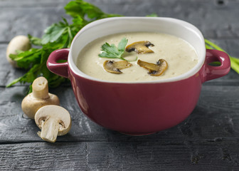 Cream soup of mushrooms with herbs on a wooden table. The decoration of raw mushrooms.