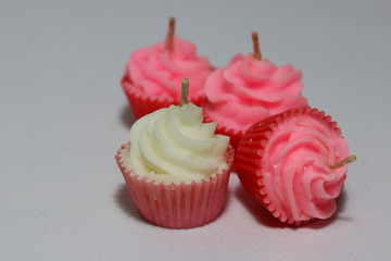 White and three pink candles in cupcake shape put on light grey background. it is a wax with a central wick that is lit to produce light as it burns.