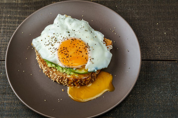 sandwich with avocado and a fried egg on a brown plate on a rustic wood table.