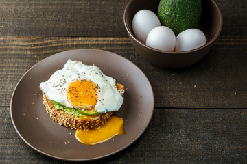 sandwich with avocado and a fried egg on a brown plate on a rustic wood table.