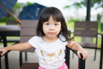 Asian little cute girl with black hair sit on the chair outdoor waiting her Dad.