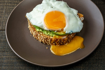sandwich with avocado and a fried egg on a brown plate on a rustic wood table.