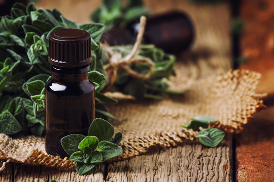 Organic essential oregano oil in a glass jar and a bunch of fresh marjoram, vintage wooden background, selective focus