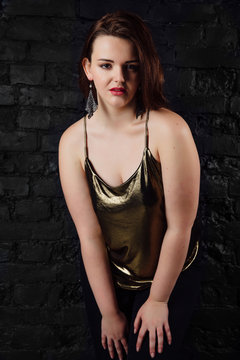 plus size model in a gold blouse and black jeans on a brick loft background.