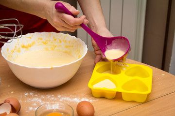 Ready for cakes. The woman's hand pours the ingredient for cakes into the mold