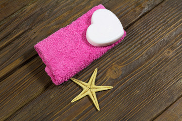 Obraz na płótnie Canvas Soap in the shape of a heart on a pink towel. Wooden background