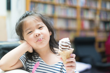 Happy Little asian girl eating soft cream or ice cream and she sit on sofa in living room.