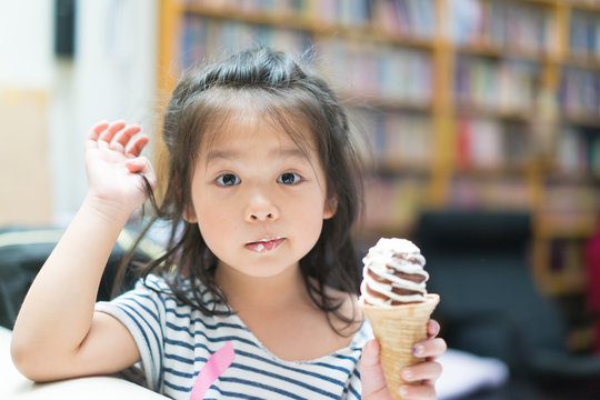 Happy Little Asian Girl Eating Soft Cream Or Ice Cream And She Sit On Sofa In Living Room.